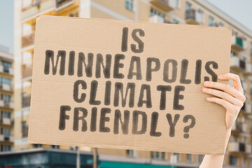 The question " Is Minneapolis climate-friendly? " is on a banner in men's hands with blurred background. Support. Team. Activist. Urban. Sunset. Carbon. Ecology. Energy. New. Clean. Warming. Waste