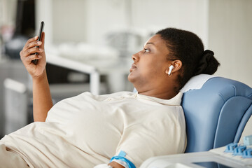 Side view of black young woman giving blood while laying in chair at blood donation center and...