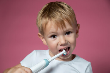 Smiling caucasian little boy cleaning his teeth with electric sonic toothbrush