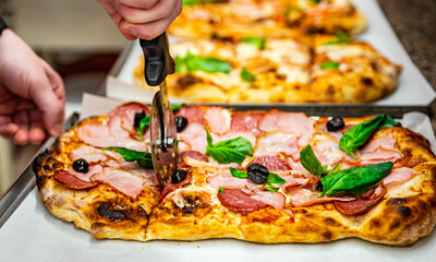 chef hand with cutter cutting roman pizza to pieces at pizzeria - obrazy, fototapety, plakaty