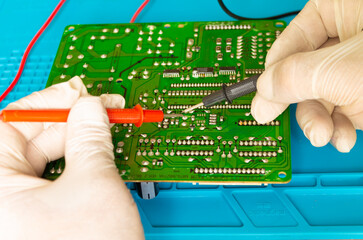 Gloved technician checks circuit board details with multimeter,