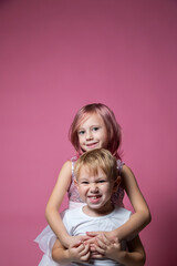 Fototapeta na wymiar Caucasian brother and sister ,hugging on camera on pink background studio shot.