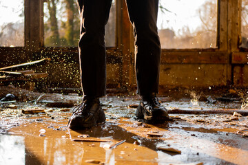 Male legs in black pants and sneakers among the puddle and frozen drops in a flooded, destroyed and...