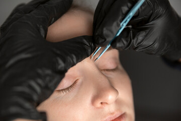 Portrait of young woman on the procedure of eyebrow correction. Cosmetologist in black gloves...