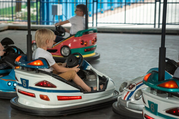 Obraz premium Young drivers having fun at children playground on go kart race. Children driving bumper car in the amusement park.