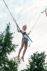 Blond boy jumping in an amusement park on the ropes high into sky. Child has fun in the theme park.