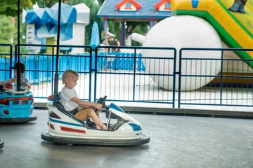 Deurstickers Little boy driving bumper car in the amusement park. Young drivers having fun at children playground on go kart race. © somemeans