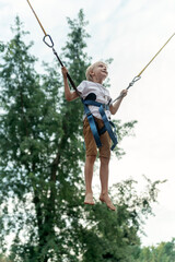 Blond boy jumping on trampoline in an amusement park. Child frolics and jumps high. Vertical frame.