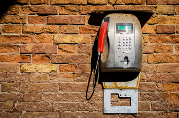 Un vecchio telefono pubblico ormai inutilizzabile appeso a un muro