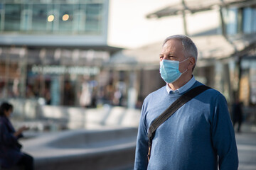 Senior man walking outdoor while wearing a protective mask against coronavirus