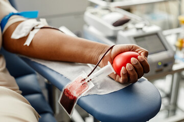 Closeup of black woman donating blood focus on hand holding red ball with tubing, copy space - obrazy, fototapety, plakaty