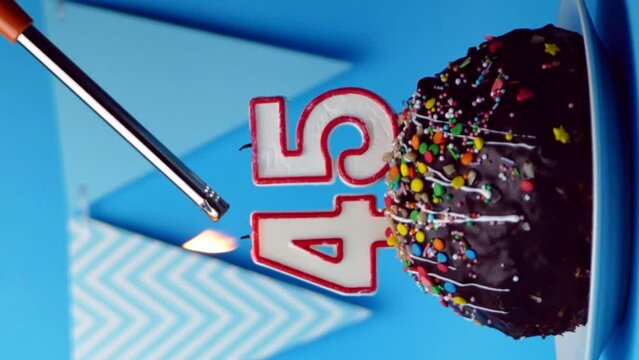 chocolate birthday cake with a burning candle number forty five, 45 on a blue background.vertical screen.