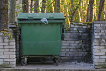 A large green plastic trash can in a public park, a plastic green trash can located in the garden, a large green plastic trash can close-up. Garbage collection in the designated place.