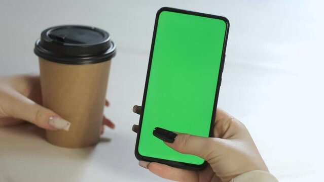 paper cup for coffee. Young female hands using green screen smartphone sitting in cafe drinking coffee. Online business communication. Chroma Key mockup. Social network. Internet chatting.