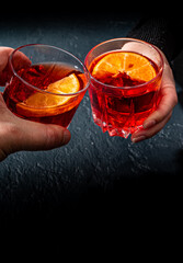 Close up of mens and women's hands clinking the glasses with Negroni cocktails on a black background.