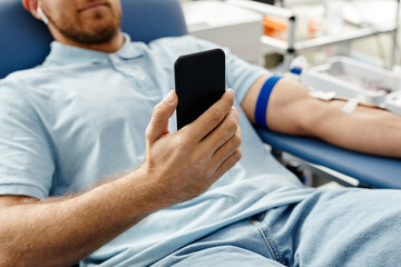 Close up of young man donating blood while lying in comfortable chair at med center and holding...