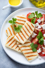 White plate with slices of grilled halloumi cheese, tomatoes and fresh parsley, vertical shot, selective focus, close-up