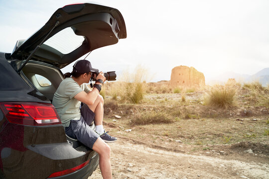 asian photographer sitting at edge of trunk taking picture at a historical site