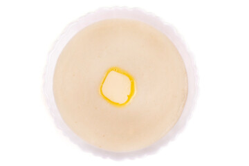 Semolina porridge with a piece of butter in a plate on a white isolated background. View from above.