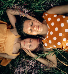 Happy family mom and daughter hug and lie on the ground on the grass in flowers, looking at the...