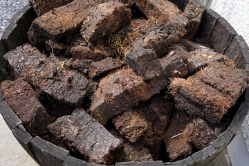 Dried lumps of peat in front of a whisky distillery. Peat is used to dry the malted barley. It...
