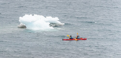 2 Personen paddeln mit einem roten Kanu durch die Abgeschiedenheit der Antarktis,  ganz nah vorbei...