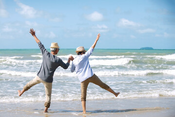 Asian senior couple wearing hat with sunglasses  holding hands dancing  walking on the beach