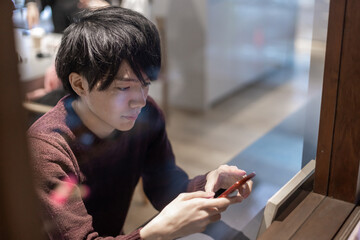 カフェの窓辺でスマートフォンを操作する20代男性