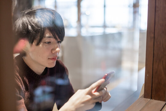 カフェの窓辺でスマートフォンを操作する20代男性