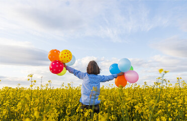 girl in a yellow field with balloons in her hands