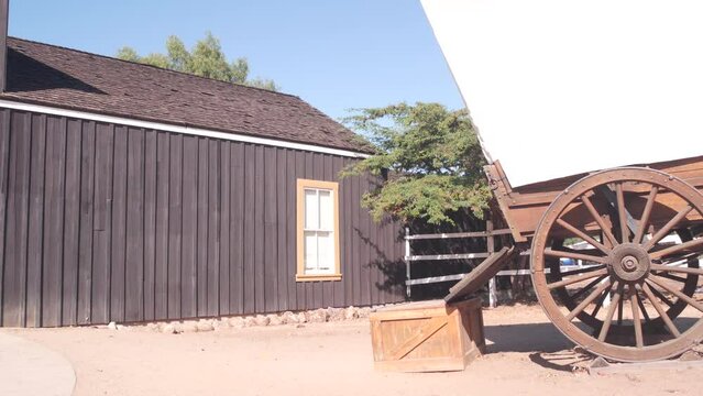 Old wooden retro covered wagon on wheels, wild west pioneer ranch. Western historic retro cart, traditional vintage transport. Rural house wall, building exterior. Countryside farm or cowboy saloon.