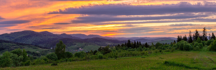 Obraz premium Spring panorama of the Carpathian Mountains with gentle greenery and enchanting sky at sunset. Panorama of mountains for wallpaper and design.