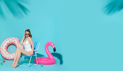 Happy woman chilling in lounge chair near flamingo rubber ring on blue copy space background. woman...