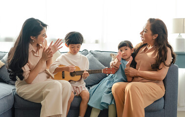 Happy Asian family grandchild with grandmother playing guitar and singing a song together at home.