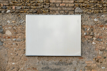 Cartello rettangolare bianco appeso a vecchio muro di pietra e mattoncino. Fotografia orizzontale.