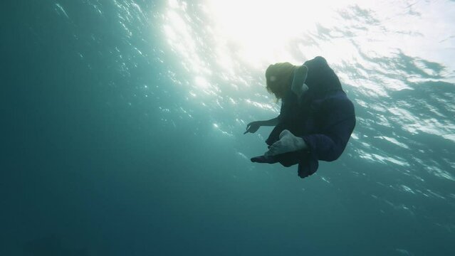 beautiful woman in flowing dress floats underwater dark background, she swims to surface of water, dancing in pristine blue ocean water, amazing snorkeling adventure. Armature freediver girl diving