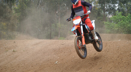 Pessoa a fazer motocross, em velocidade com a mota no ar depois de um salto, piso de terra batida