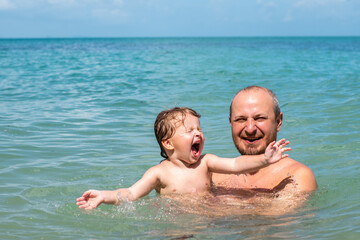 Dad and his little daughter are swimming in the sea. The child screams with delight. Emotions of happiness in children. Family holidays