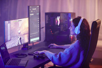 Young adult Caucasian woman spending free time playing shooter video game on desktop computer in living room at night