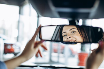 Woman driver sitting in car and looking into mirror