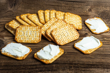 Crackers spread with cheese as a light snack on a wooden plank