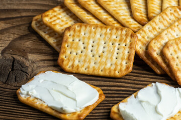 Crackers spread with cheese as a light snack on a wooden plank