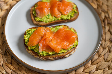 Toasted bread with mashed avocado and smoked salmon on grey plate