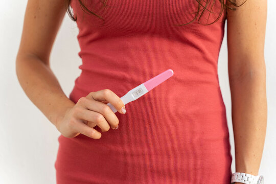 mujer embarazada ense&ntilde;ando un test o prueba de embarazo positivo con un vestido rosa