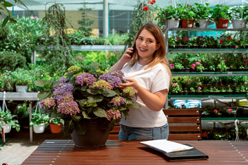 Portrait of garden center manager working with flowers and talking on phone