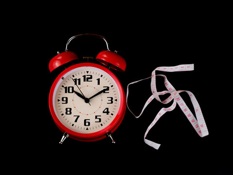 A red clock and ruler tailor sewing cloth measure tape. Isolated with black background. Diet concept.