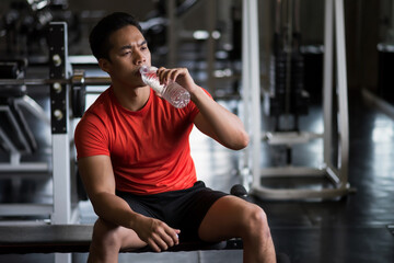 Young Asian strong muscular man drink water in fitness gym