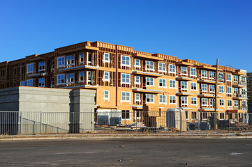 Wood-framed multifamily building under construction with scaffolding, concrete blocks, and safety fencing, illustrating urban housing development and construction industry progress.