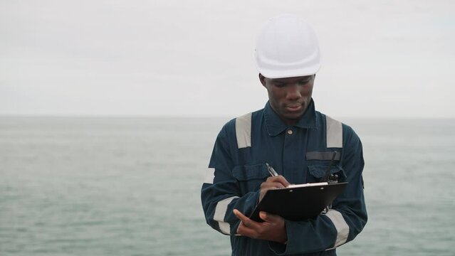 Black seaman taking notes near sea
