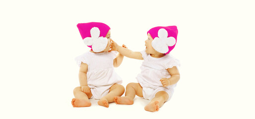 Portrait of two twin babies looking at each other playing together wearing pink winter knitted hats on white background